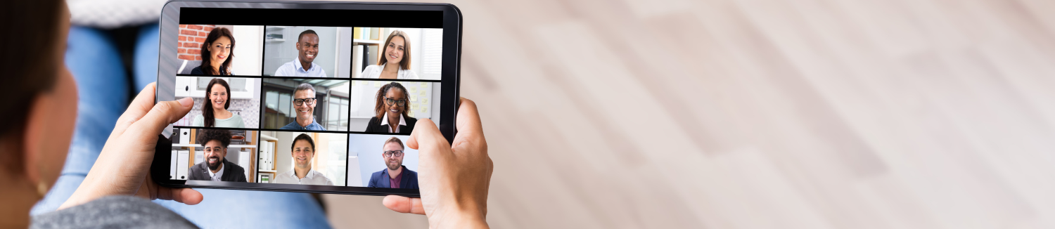 A person holds a tablet displaying a video conference with nine participants in a grid layout.